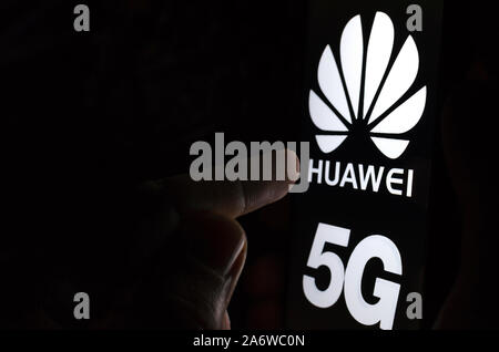 Huawei 5G Logo auf einem Bildschirm des Smartphones in einem dunklen Raum und einen Finger zu berühren. Stockfoto