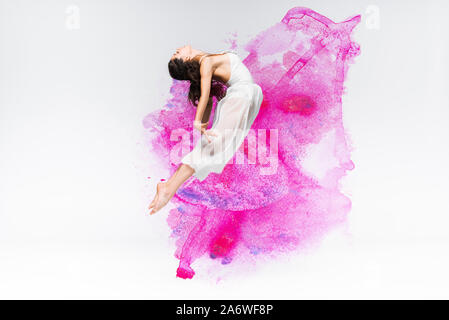 Schöne Ballerina in weißem Kleid tanzen in lila und rosa Farbe spritzt und verschüttete Flüssigkeiten auf grauem Hintergrund Stockfoto