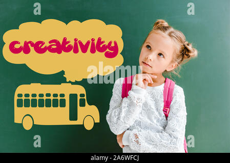Nachdenklich Zicklein stehend mit Rucksack in der Nähe von schiefertafel mit Schulbus und Kreativität Schriftzüge auf Grün Stockfoto