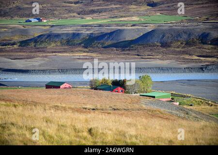 Fellabaer, Island. Bauernhöfe eingebettet in einem Tal auf der anderen Seite eines Flusses von gletschersee/river Logurinn unter Bergen in der Nähe von Fellabaer. Stockfoto