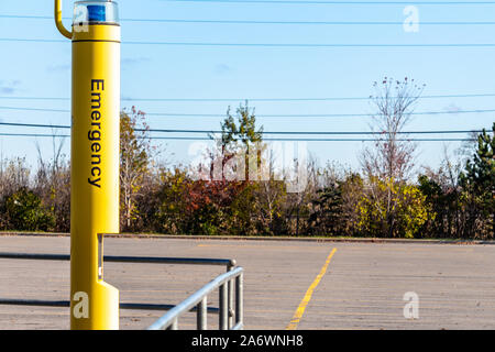 Eine gelbe Pole stehen in einem öffentlichen Parkplatz verfügt über ein blaues Licht und eine Gegensprechanlage für Hilfe anfordert. Das Wort "Notfall" auf der Seite angezeigt. Stockfoto