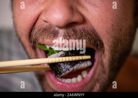 Nahaufnahme eines Mundes eines bärtigen kaukasischen Mann essen Hausgemachte sashimi Sushi Roll mit Stäbchen Stockfoto