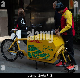 DHL-Mitarbeiter an der Londoner High Street gesehen, die Post auf einer elektrisch betriebenen Lieferung Bike. Stockfoto