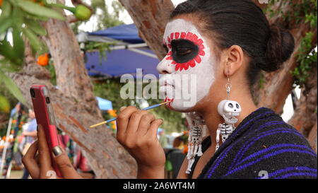 Ein junger spanischer Frau setzt auf Sugar Skull Make-up können Sie über Ihr Handy Kamera wie ein Spiegel. Stockfoto