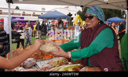 Eine lächelnde Frau in einem Marktstand bietet den Geschmack von Pan de Muerto an einem Tag der Toten. Stockfoto