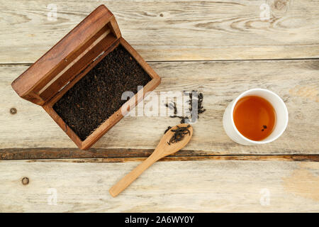 Schwarz indischen Tee in einer Box, auf einen Löffel und in einem Glas auf einem hölzernen Hintergrund gebraut. Der Blick von oben Stockfoto