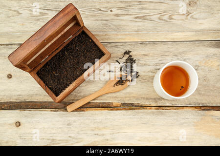Schwarz indischen Tee in einer Box, auf einen Löffel und in einem Glas auf einem hölzernen Hintergrund gebraut. Der Blick von oben Stockfoto