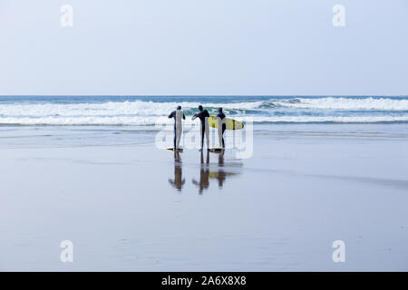 Surfer, mit Surfbrettern, an einem nassen Strand in Polzeath, Cornwall, Großbritannien Stockfoto