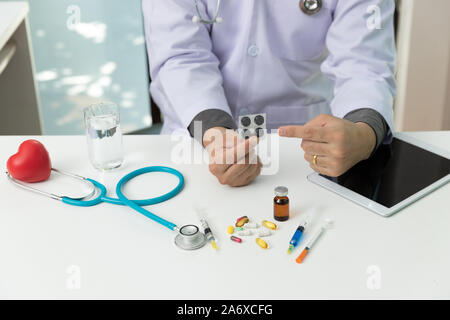 Arzt holding Medizin Pillen in die Hand und erklärte Medikation mit sortierten pharmazeutische Medizin Pillen auf Tisch Stockfoto