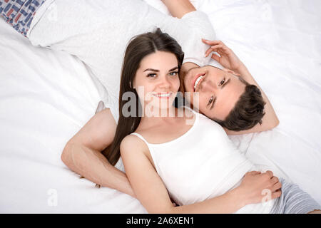 Bedtime. Junges Paar liegend auf Bett Draufsicht isoliert auf weißem Umarmen lächelt Fröhlich Stockfoto
