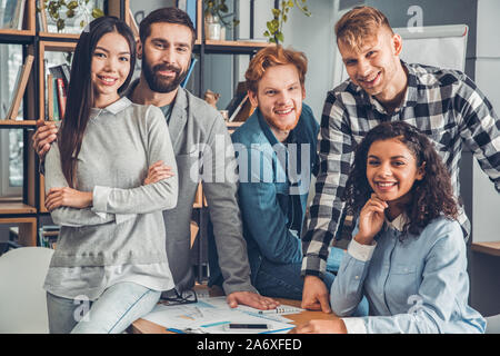 Startupers zusammen arbeiten im Büro umarmen suchen Kamera freudige Stockfoto