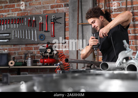 Mann in Home Werkstatt garage Arbeit Bohren von Metall mit Bohrer, Reparatur eiserne Leitung auf der Werkbank voller Schlüssel, Heimwerker- und craft-Konzept Stockfoto