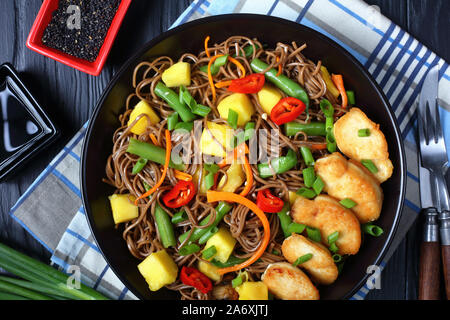 In der Nähe von Huhn und Mango Soba Nudelsalat mit Gedünsteten grünen Bohnen, Karotten, Paprika und Frühlingszwiebeln in einem schwarzen Schüssel auf Holzkasten Stockfoto