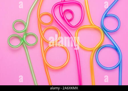 Abstrakte bunten Hintergrund von gekrümmten cocktail Strohhalme. Kunststoff Spirale multicolor Rohre auf rosa Papier. Spaß, Stimmung. Minimales Design. Stockfoto