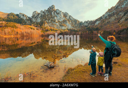 Mutter und Kinder am Ufer des Laudachsee, Österreich, mit den beeindruckenden Katzenstein steigen in den Hintergrund und im kristallklaren Wasser spiegelt Stockfoto