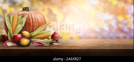 Ein Thanksgiving Feier Tabelle der Kürbisse, Äpfel, Birnen und Maiskolben mit Herbst Sonnenuntergang Laub im Hintergrund. Stockfoto