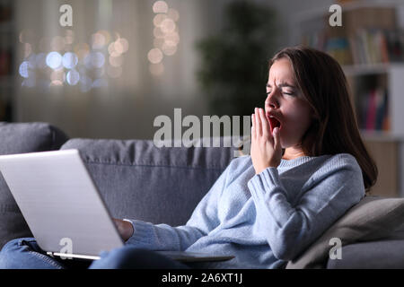 Müde Frau mit Laptop Gähnen sitzen auf einer Couch in der Nacht zu Hause Stockfoto