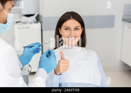 Zufriedene junge Dame im Zahnarztstuhl, Daumen hoch Stockfoto