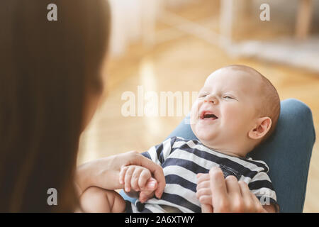 Lustige neugeborenes Baby lacht während auf Mutters Schoß liegend Stockfoto