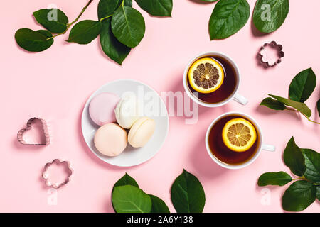 Kaffee Bremsen Set - zwei Tassen Tee mit Zitrone und Rosenblüten mit Marshmallows auf einem rosa Hintergrund. Flach, Ansicht von oben. Stockfoto