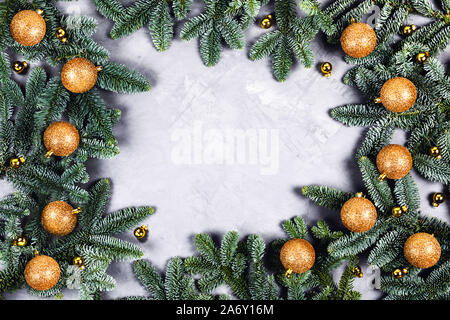 Weihnachten grauen Hintergrund mit grünen Tanne brunches, golden und glänzenden Weihnachtskugeln mit Platz für den Text. Flach, Ansicht von oben. Stockfoto