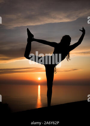 Silhouette der junge und sportliche Frau Yoga (stehend Maßstab darstellen) mit romantischen Sonnenuntergang und das Meer im Hintergrund an den goldenen Stunde Stockfoto