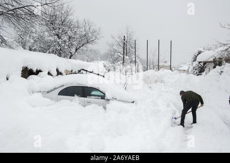 Nicht erkennbare Mann Reinigung der Schnee vor einem Auto, im Schnee bedeckt. Personen und Fahrzeug bilden. Reinigung Schnee, Schneefall im Winter Stockfoto