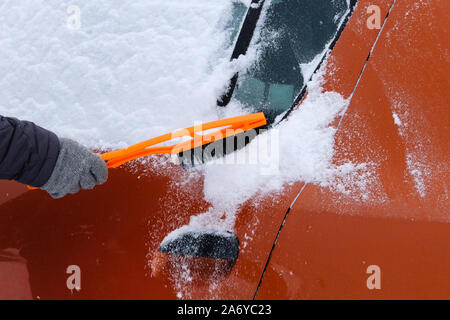 Auto mit Schnee bedeckt. Bürste in mans hand. Mann in grau Handschuhe ist Bürsten orange Auto vom Schnee. Stockfoto