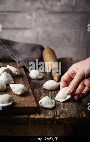 Der Prozess der Herstellung hausgemachte Knödel. Raw hausgemachte Knödel mit Fleisch auf einem Holzbrett mit Frauen Hände Stockfoto
