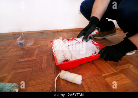 Bauarbeiter und Maler mit Handschuhen hält weiße Walze Pinsel in der hand und Mixe weiß mit roten extrahieren und Pigment Farbe in der Schüssel. Stockfoto
