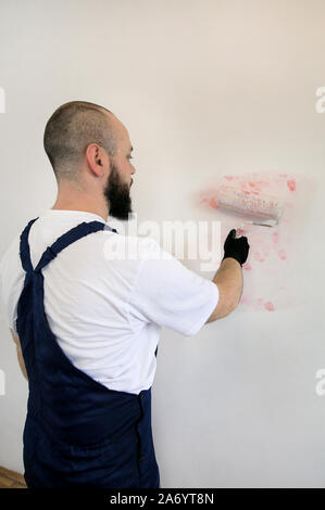 Bauarbeiter tun beenden Renovierung im Apartment. Professionelle Maler Auftragnehmer mit weißer Farbe bürstenrolle Gemälde an der Wand. Stockfoto