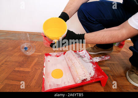 Bauarbeiter tun beenden Renovierung im Apartment. Maler mit schwarzen Handschuhen gießt gelbe Farbe von der Schaufel in die roten Schüssel für Farbe mischen. Stockfoto