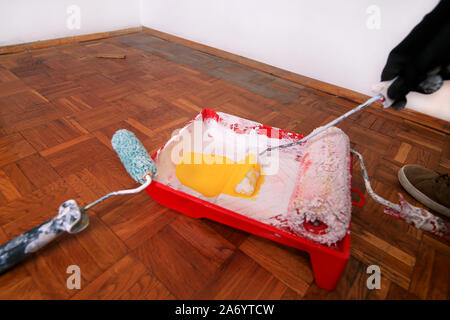 Bauarbeiter und Maler mit Handschuhen hält Bürstenrolle Farbe in der Hand und Mixe gelbe Farbe im Container- und roten Schüssel für Farbmischung. Stockfoto
