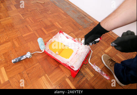Bauarbeiter und Maler mit Handschuhen hält Bürstenrolle Farbe in der Hand und Mixe gelbe Farbe im Container- und roten Schüssel für Farbmischung. Stockfoto