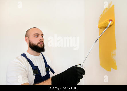 Bauarbeiter und Handwerker tun beenden Renovierung im Apartment. Maler mit paint Bürstenrolle Anstrich der Wand mit der Farbe gelb. Stockfoto