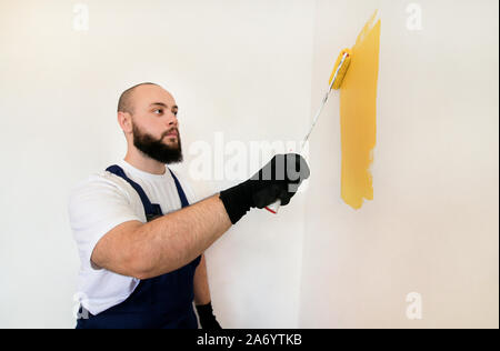 Bauarbeiter und Handwerker tun beenden Renovierung im Apartment. Maler mit paint Bürstenrolle Anstrich der Wand mit der Farbe gelb. Stockfoto