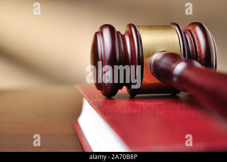 Holz Richter Hammer mit einer Brass Band um den Kopf, die auf der Oberseite von einem geschlossenen roten Gesetz Buch mit flachen Dof und Copyspace Stockfoto
