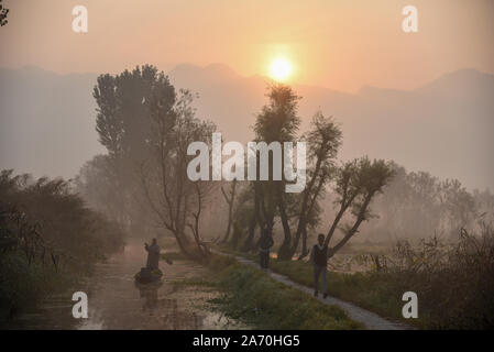 Srinagar, Jammu und Kaschmir, Indien. 29 Okt, 2019. Ein Kaschmirischen boatman Zeilen sein Boot als Menschen auf einer hölzernen Brücke am frühen Morgen in die Innenräume der Dal Lake. Kaschmir zwischen Indien und Pakistan seit der Partition und der Unabhängigkeit von Großbritannien im Jahr 1947 aufgeteilt. Die umstrittene Region ist in vollem Umfang durch beide Seiten, die drei Kriege um sie gekämpft haben behauptet. Kredit Idrees: Abbas/SOPA Images/ZUMA Draht/Alamy leben Nachrichten Stockfoto