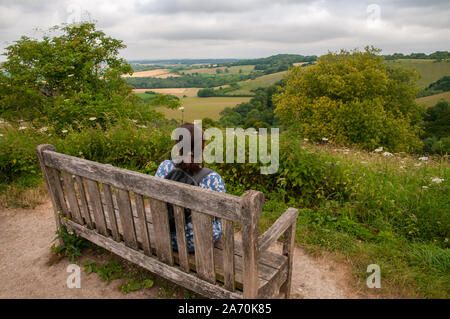 Eine Frau mittleren Alters Walker ist ein Rest während des South Downs Way zu Fuß in die Landschaft von Hampshire gerade östlich von Winchester, England. Stockfoto