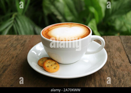 Tasse Cappuccino Kaffee mit Gebäck serviert auf hölzernen Tisch im Garten Stockfoto