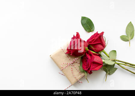 Zusammensetzung von Geschenk- und Strauß roter Rosen auf weißem Hintergrund. Happy Valentines Tag. Ansicht von oben. Copyspace Stockfoto