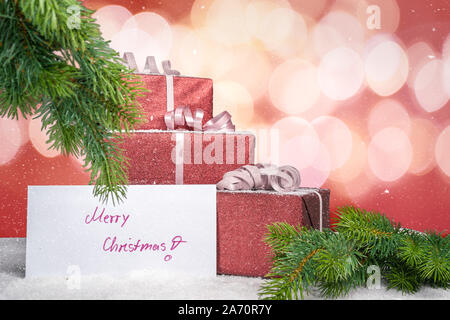 Red christmas Geschenke liegen unter dem Weihnachtsbaum und einer Grußkarte mit der Aufschrift frohe Weihnachten Stockfoto