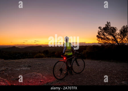 Reife weibliche Radfahrer bei Sonnenuntergang auf dem Gipfel des Alpilles, in der Nähe von San Remy, Provence, Frankreich. Stockfoto