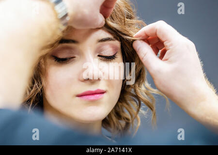 Friseur Hände sind Kontrolle junge Frau Braun Frisur auf grauem Hintergrund. Stockfoto