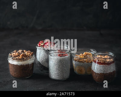 Eingestellt von Chia Pudding in verschiedenen Gläsern auf dunklen Tisch. Sortiment von Chia puding mit verschiedenen Früchten, Nüssen, Zutaten. Kopieren Sie Platz für Text. Superfood, Detox, gesunde Übernachtung Frühstück Konzept Stockfoto