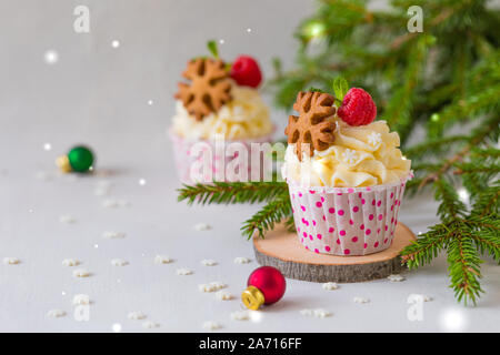Weihnachten kleine Kuchen oder Muffins mit Sahne und Himbeere, über die Fir Tree Branches Hintergrund, getönt Stockfoto
