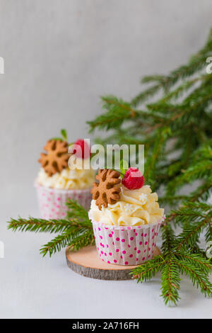 Weihnachten kleine Kuchen oder Muffins mit Sahne und Himbeere, über die Fir Tree Branches Hintergrund, getönt Stockfoto