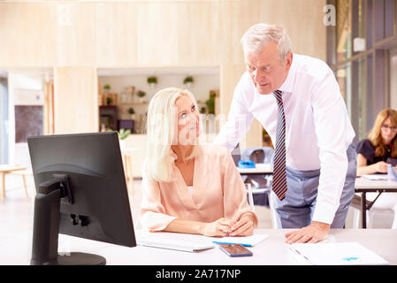 Screenshot des mittleren Alters Finanz Buchhalter Geschäftsfrau im Büro Schreibtisch hinter ihrem Computer sitzen, während die älteren Geschäftsmann stand neben ihr und c Stockfoto