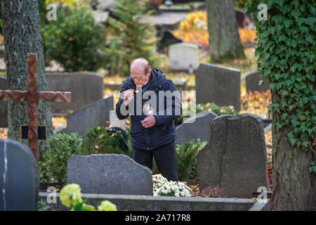 Der Mann besucht die Gräber von Angehörigen und leuchtet eine Kerze Friedhof in Vilnius, Litauen. Die Gräber sind mit Blumen und Kerzen Stockfoto