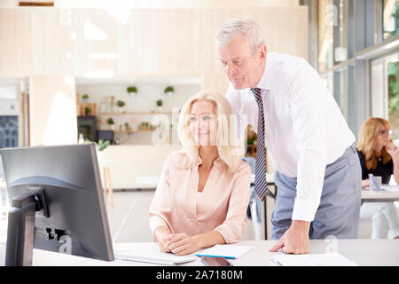 Screenshot des mittleren Alters Finanz Buchhalter Geschäftsfrau im Büro Schreibtisch hinter ihrem Computer sitzen, während die älteren Geschäftsmann stand neben ihr und c Stockfoto